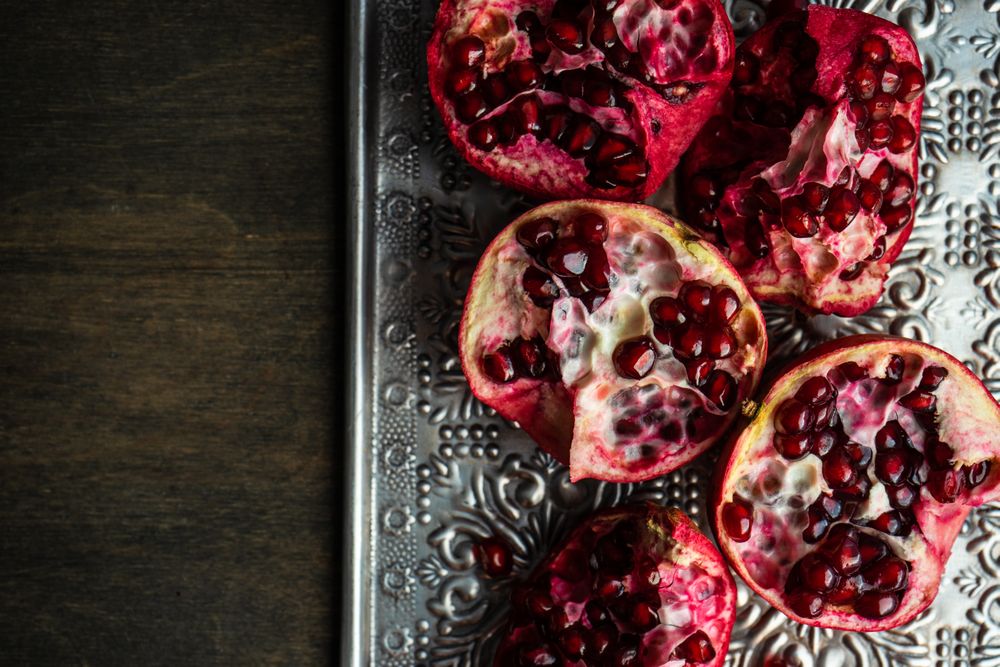 Top view of open pomegranates on ornate silver trey