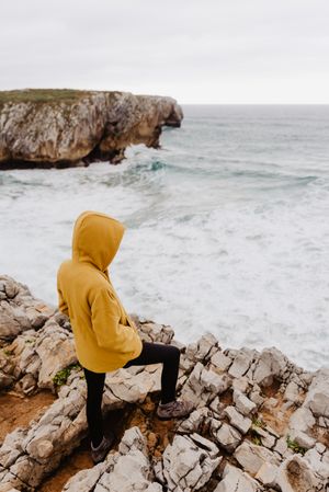 Person in yellow hoodie on stony shore