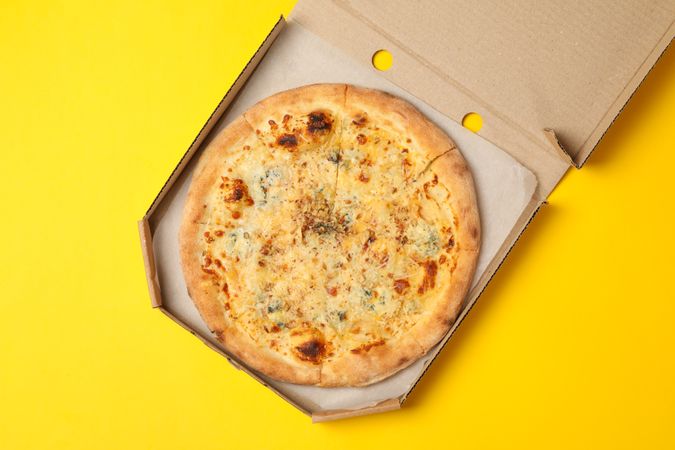 Cheese pizza in carton box on yellow background