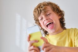 Happy boy taking selfie on smartphone on light background