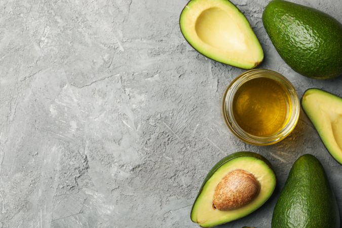 Ripe fresh avocado and oil on gray background, top view