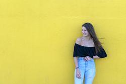 Smiling woman leaning on yellow wall on a sunny day