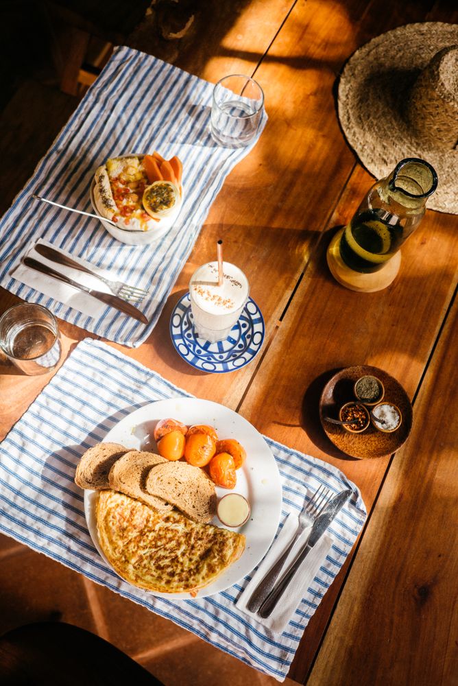 Table set with omelette breakfast and bowl of fresh fruit and yogurt, vertical