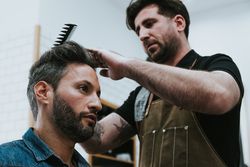 Barber combing hair to man in salon