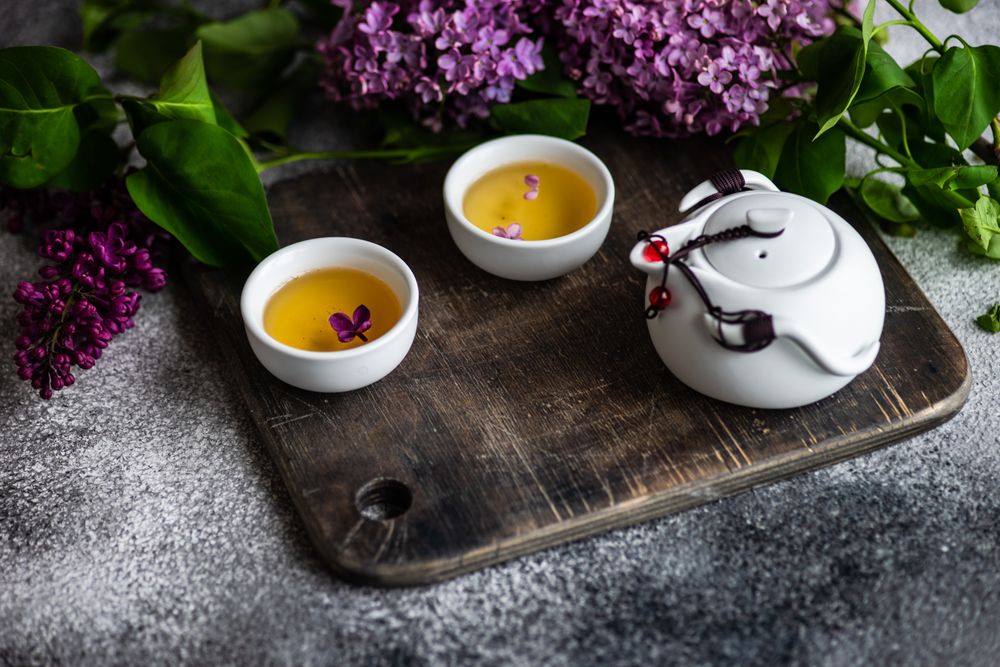 Teapot with cups with delicate tea and pink flowers