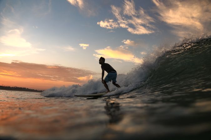 Man on surf board on waving water at sunset