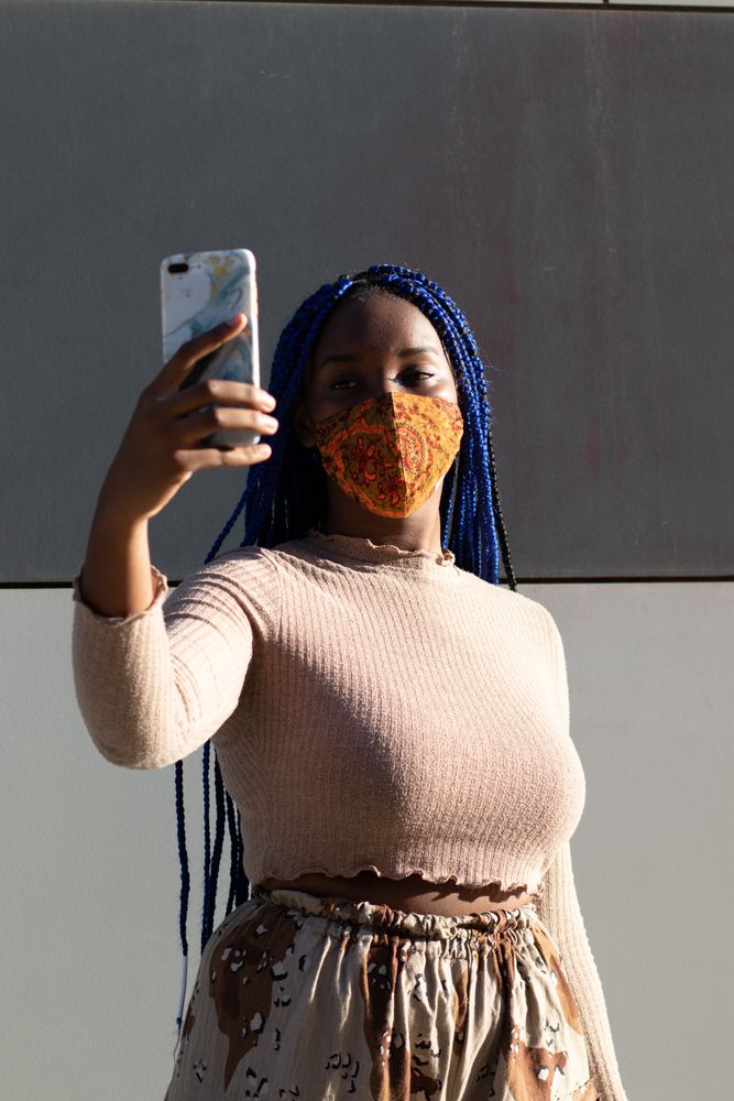 Stylish Black woman taking selfie in mask
