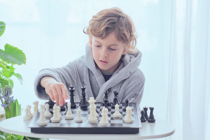 Focused preteen boy sitting at table and playing chess