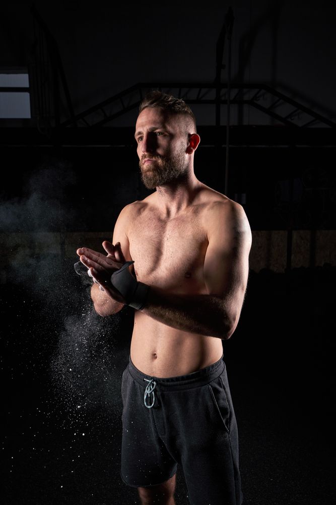 Shirtless sportsman clasping hands in dark room