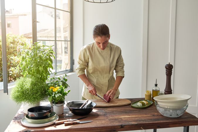 Serious woman cutting meat at home