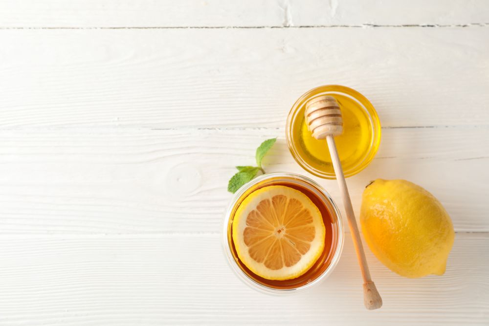 Glass of tea with lemon, mint, honey and dipper on wooden background, top view