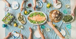 Group of people serving themselves fish, on blue patterned table with wine and side dishes