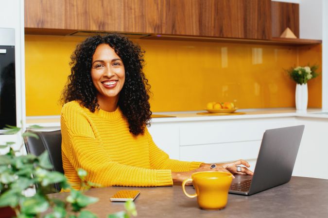 Woman in colorful kitchen smiling while looking up her laptop