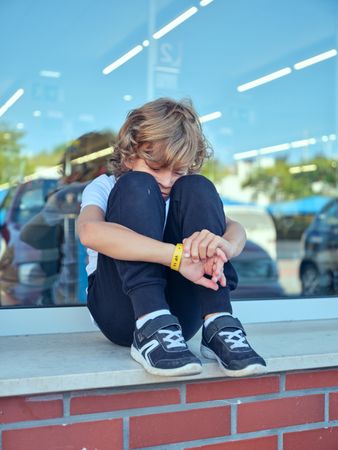Sad boy sitting on windowsill in city