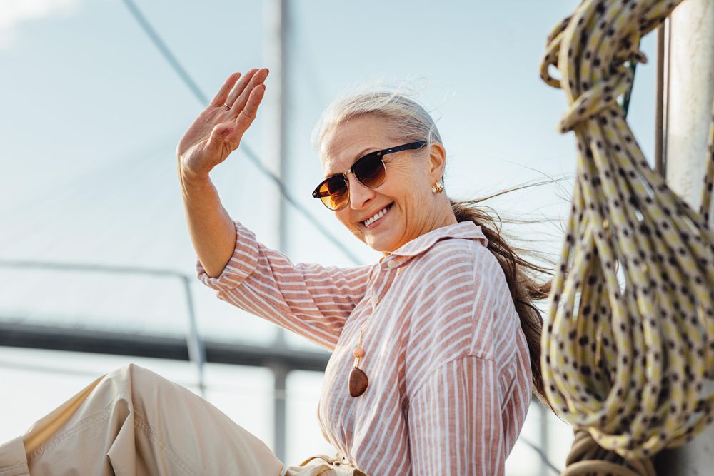 Stylish older woman sitting on a yacht bow waving