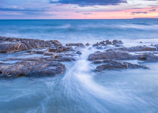 Sea waving near rough rocks during sunset