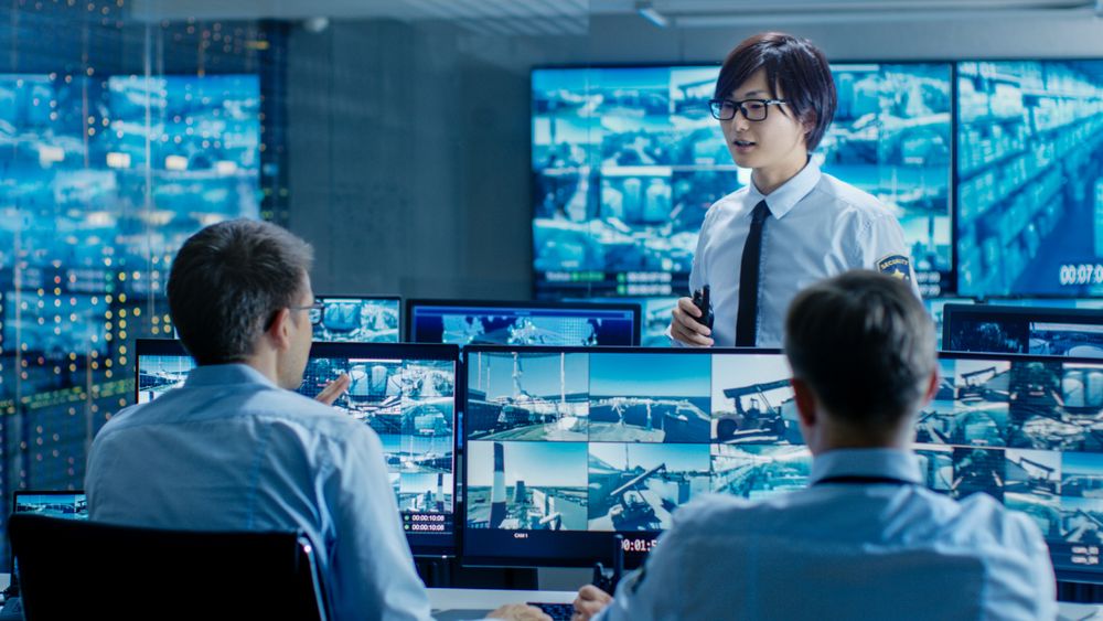In the Security Control Room Chief Surveillance Officer Briefs Two of His Subordinates.