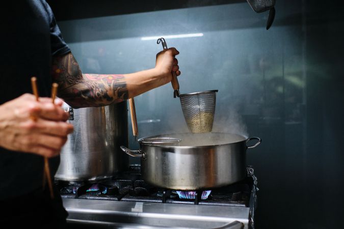 Crop faceless man cooking noodles in kitchen