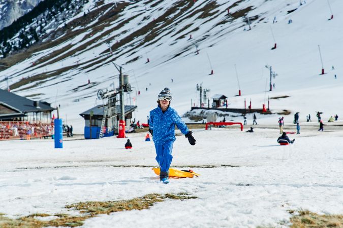 Boy with sledge walking near snowy mountain
