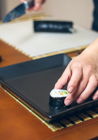 Hands of chef placing avocado sushi roll on plate