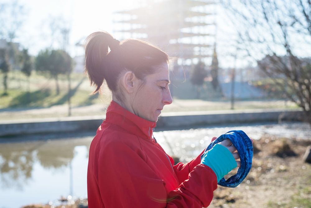 Side view of woman adjusting ear warmers outdoors in the grass on sunny fall day