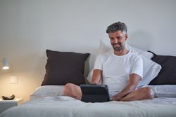 Cheerful businessman browsing tablet in bed