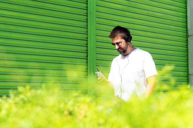 Man checking phone walking in front of green shutters