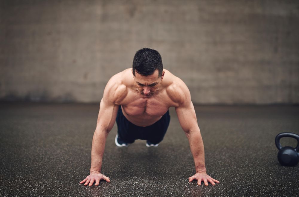 Fit shirtless man doing planks in concrete space