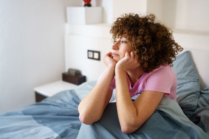 Contemplative woman relaxing under blue sheet in bed
