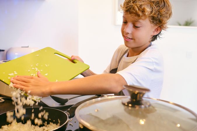 Crop boy putting chopped onion in pan at home