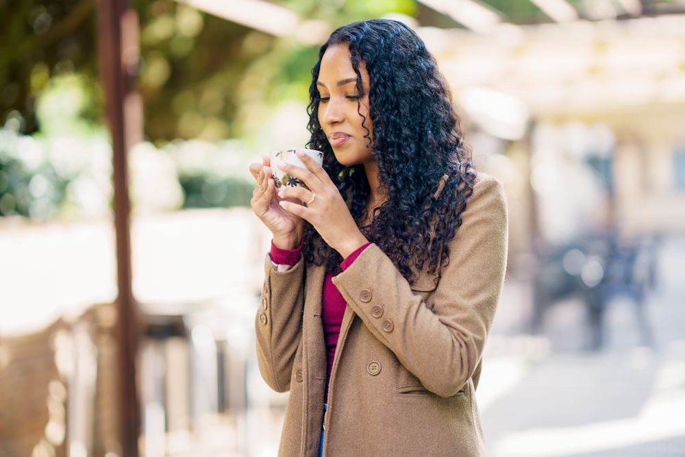 A woman is savoring a warm beverage, such as coffee or tea, while enjoying the outdoors