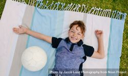 Top view of a boy lying on a blanket laid out in a park 5Xr3Kr