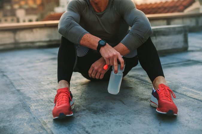 Muscular man in red trainers sitting with water bottle on roof