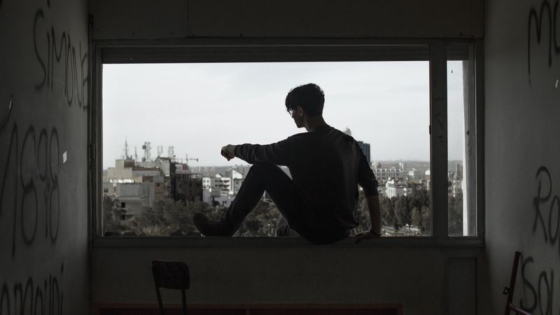 Man sitting on an open window viewing city during daytime
