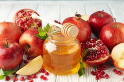 Fall fruit of pomegranates and apples with pot of honey on wooden table