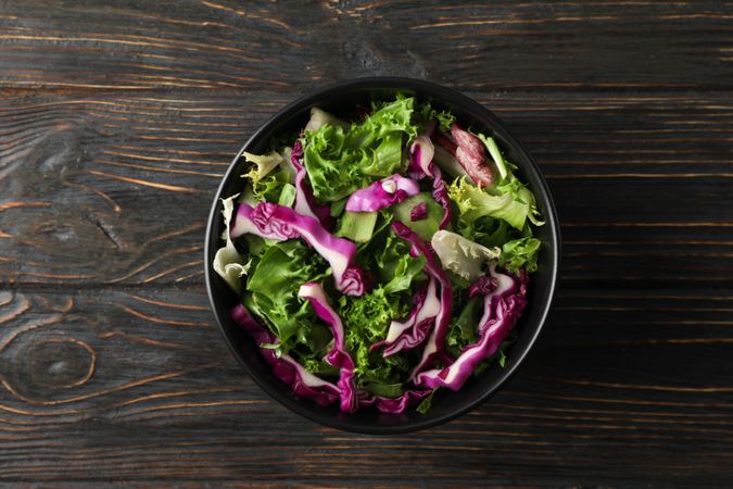 bowl with fresh vegetable slices on wooden background, top view