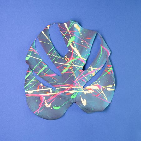 Monstera leaf painted in neon colors on pastel blue background