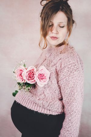 Side view of pregnant woman in knit sweater holding pink rose bouquet