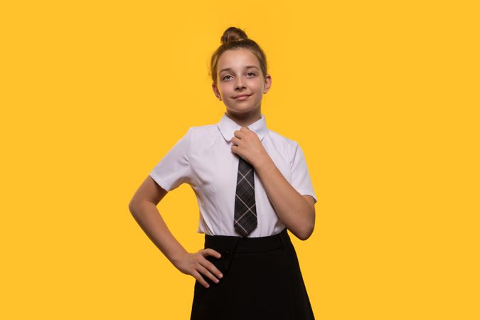 Teen girl adjusting tie in school uniform, posing confidently