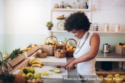Young woman working at juice bar and cutting fruits bDaL80