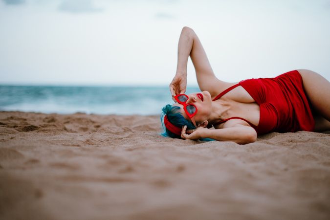 Relaxed woman in bright stylish swimsuit lying on sandy beach