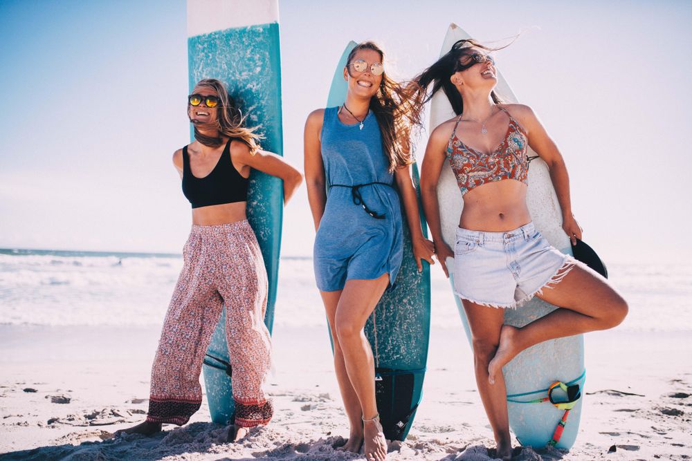Group of young women standing with surfboards on their back at the beach