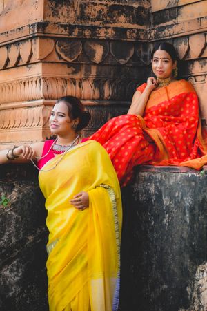 Two Indian woman in saris beside a carved wall