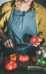 Woman in yellow holding large halved tomatoes and knife