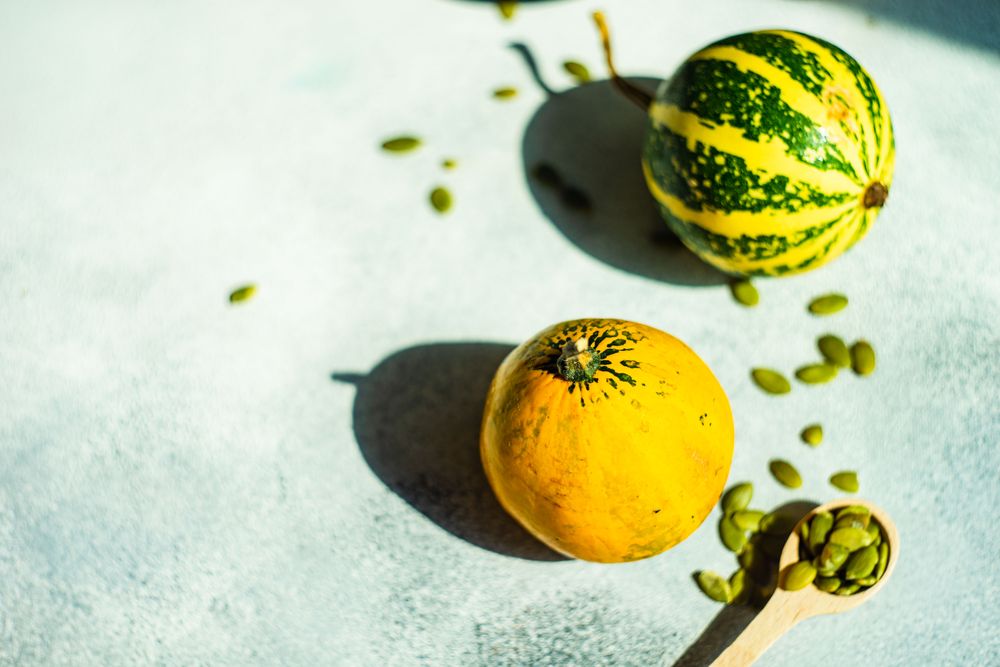 Two colorful mini squash on bright counter top with spoons of seeds
