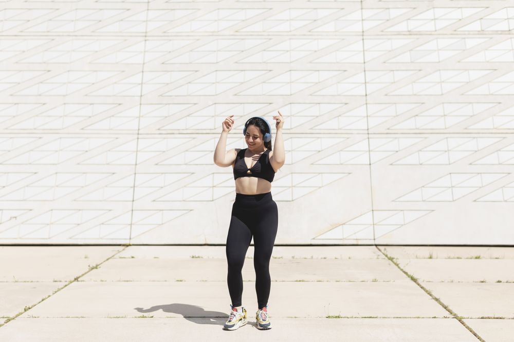 A young woman, dancing and moving, happy, while listening to music with headphones and disconnecting, to relax, after exercising