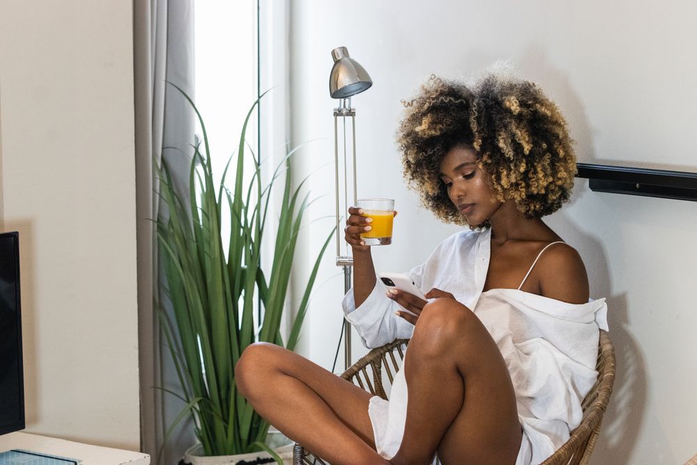 Black woman sitting on armchair and surfing smartphone