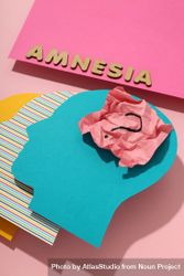 Vertical closeup of paper cut outs of colorful head on pink background with the word “Amnesia” 0J8YZ4