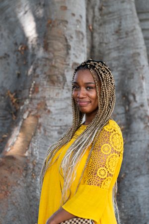 Portrait of woman with long braids standing in front of tree trunk outside