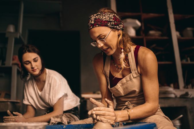 Two women at a pottery workshop making clay pots on wheel
